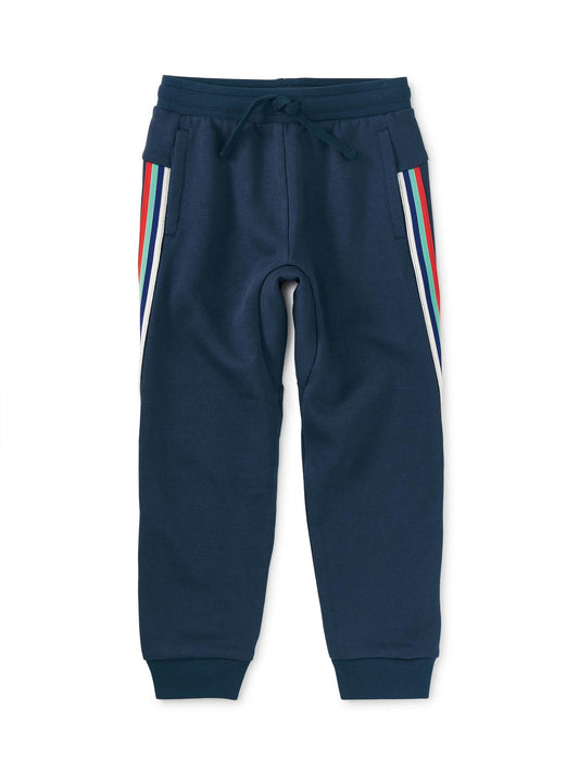 A pair of blue jogger pants for boys with contrasting white and red stripes on the legs and a drawstring waist.
