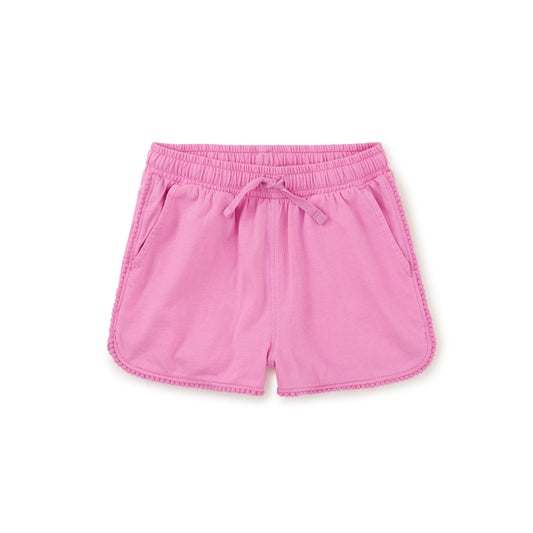 A pair of pink gym shorts with a drawstring waist and pom-pom trim, designed for children.