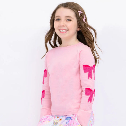 Young girl wearing a pink pajama set with bow designs on a white background