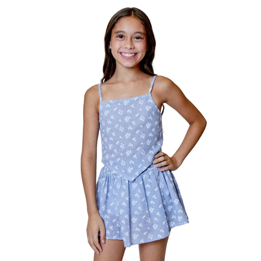 Young girl wearing a blue floral dress against a light gray background with decorative flowers.