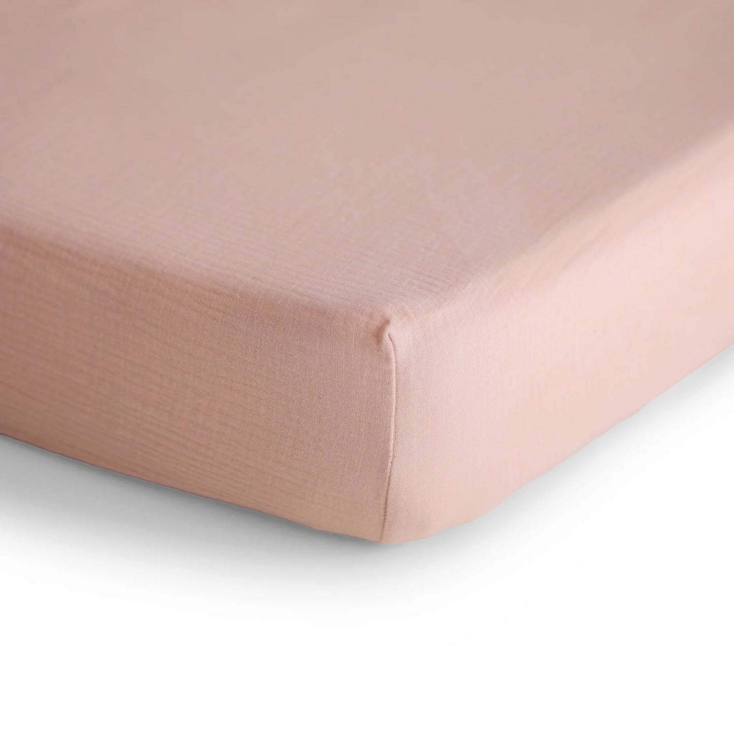 Close-up of a fitted sheet on a bed with a light pink color.