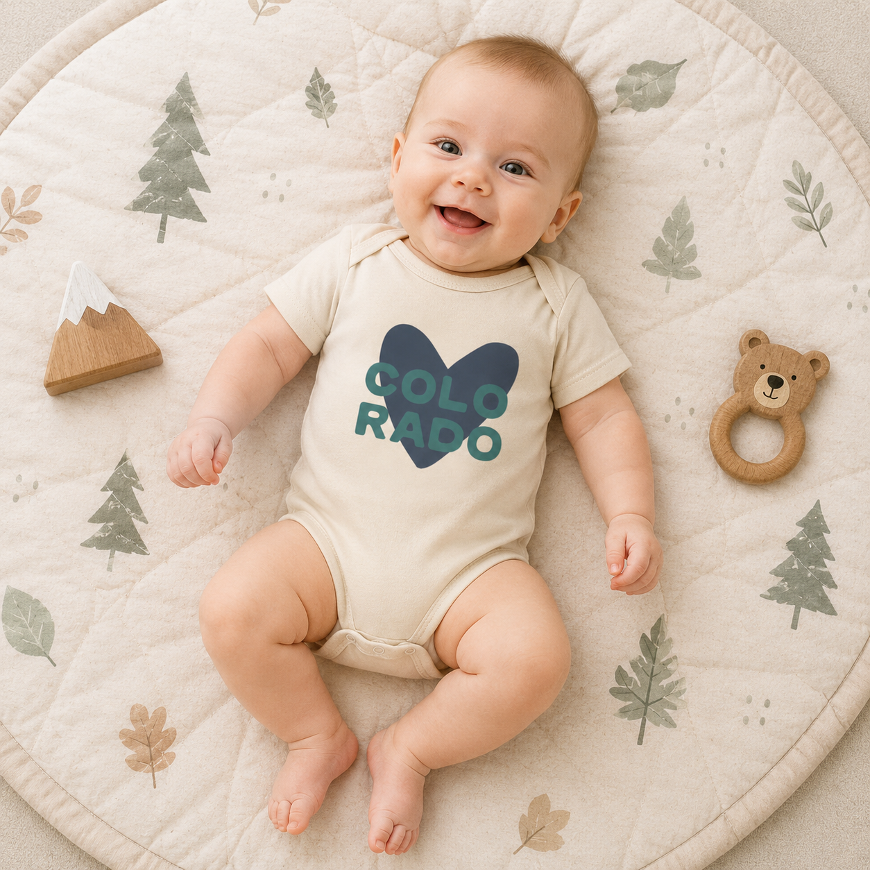 Baby wearing a beige onesie with a blue heat and the word'Colorado' printed on it.