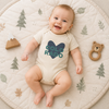Baby wearing a beige onesie with a blue heat and the word'Colorado' printed on it.