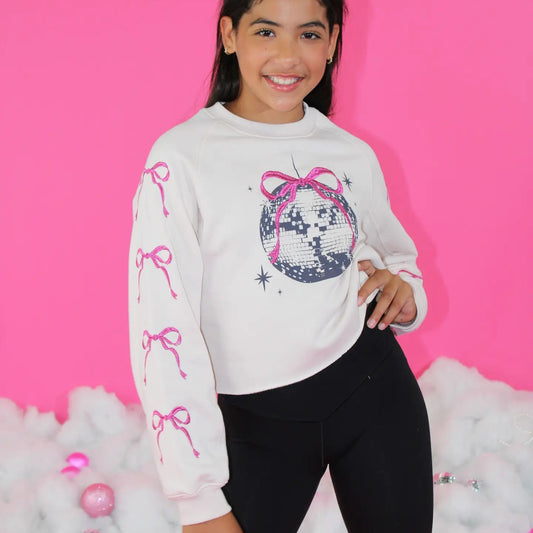 Girl wearing a white sweatshirt with pink bow designs and a disco ball graphic against a pink background.
