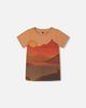 A beige t-shirt with a printed graphic of mountains and a sunset.