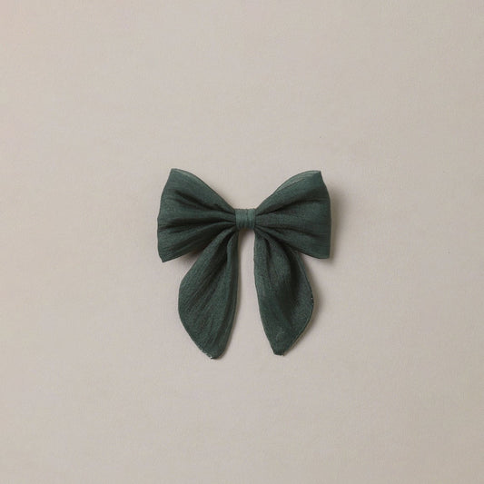 A dark green fabric bow accessory centered on a plain, warm off-white background.