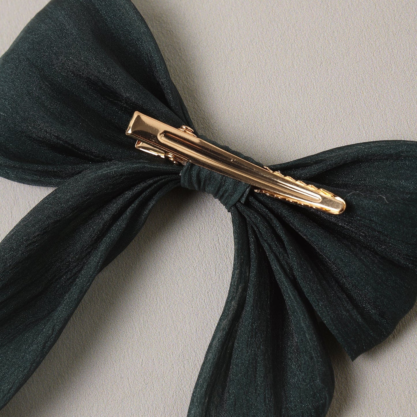 A dark forest green fabric hair bow with a gold metal hair clip, shown against a neutral light gray background.