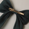 A dark forest green fabric hair bow with a gold metal hair clip, shown against a neutral light gray background.