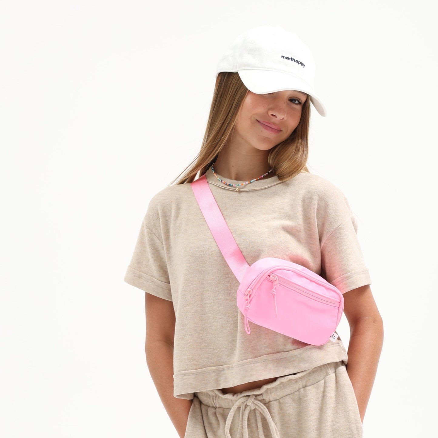 Person wearing a beige outfit with a pink fanny pack on a white background
