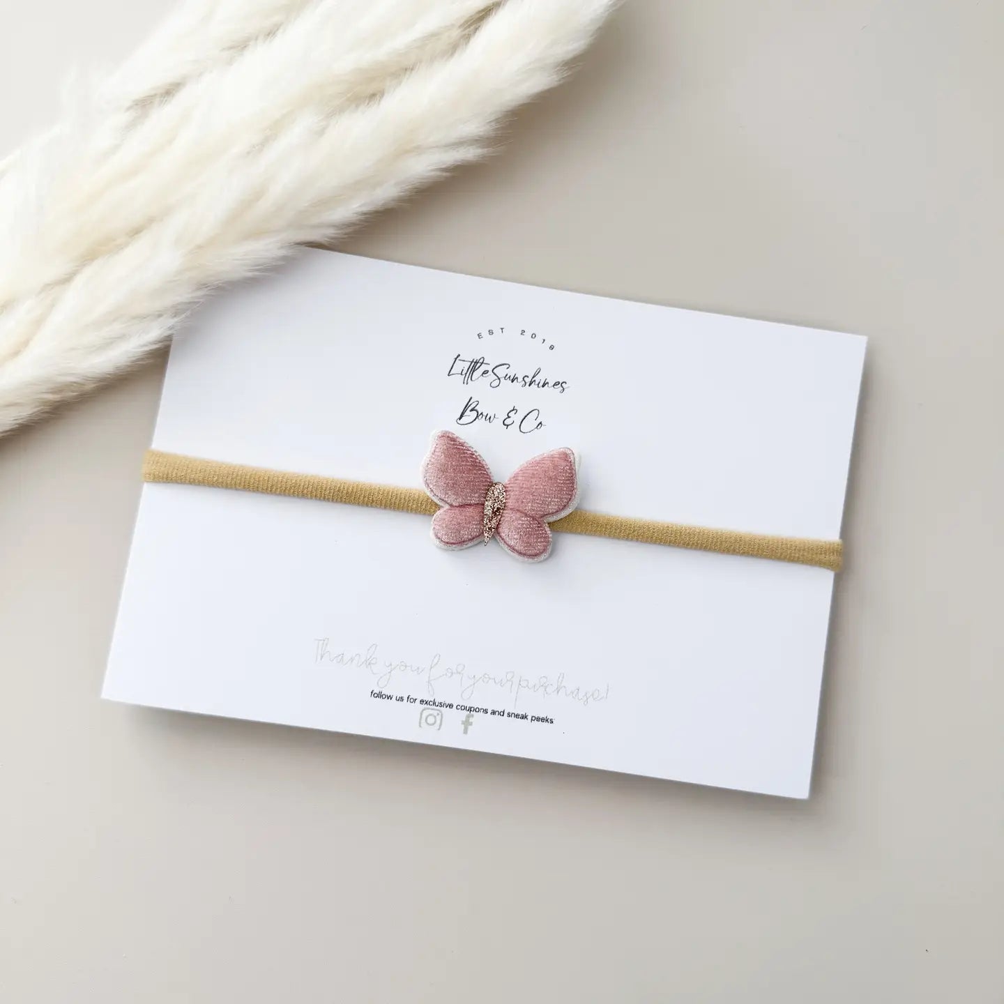 Pink butterfly hairband on a white card with 'Little Sunshine Bow Co' branding, on a beige surface.