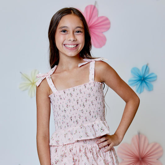 Young girl wearing a pink floral tank with decorative flowers in the background