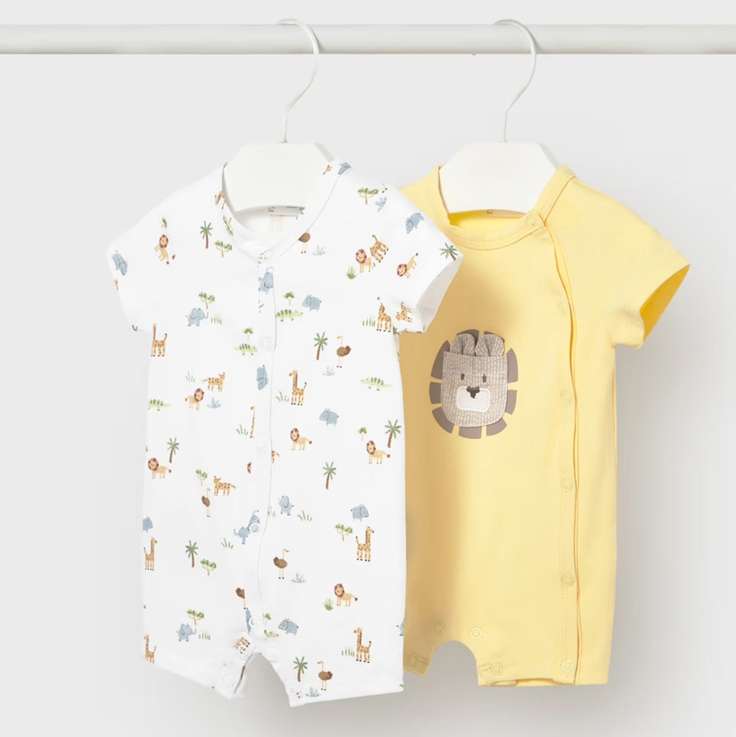 Two baby rompers, one with animal print and one yellow, hanging on a white background.