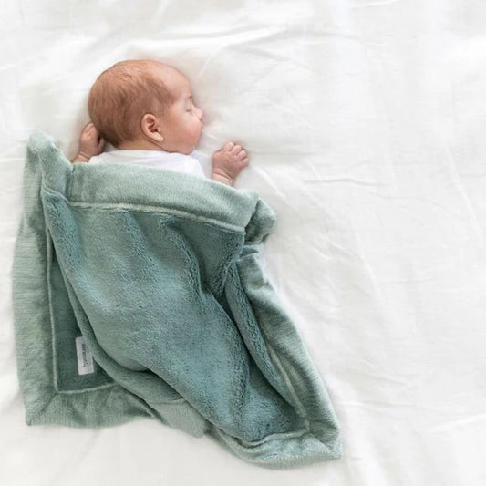 Newborn baby wrapped in a green blanket on a white surface