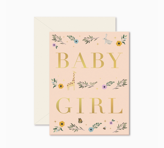 A folded greeting card with 'BABY GIRL' written in gold foil on a pink background, surrounded by floral and animal illustrations, with a beige envelope behind it.