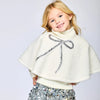 Child wearing a white sherpa poncho with a sequin bow and a silver sequin skirt on a light gray background