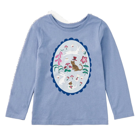 A light blue long-sleeve crewneck shirt for kids, featuring a large central graphic print of a whimsical cat and mushroom scene inside an oval frame.