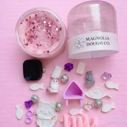 Jar of play dough with a mini kitty toy figure, featuring Magnolia Dough Co. branding.