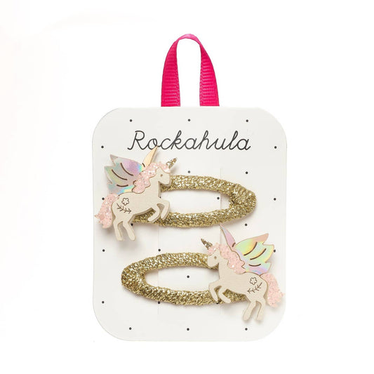A set of two gold glitter hair ties with pastel unicorn charms, presented on a white display card with a pink ribbon loop and the brand name 'Rockahula'.