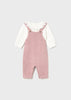 Pink knitted dungarees with a white shirt underneath on a light gray background