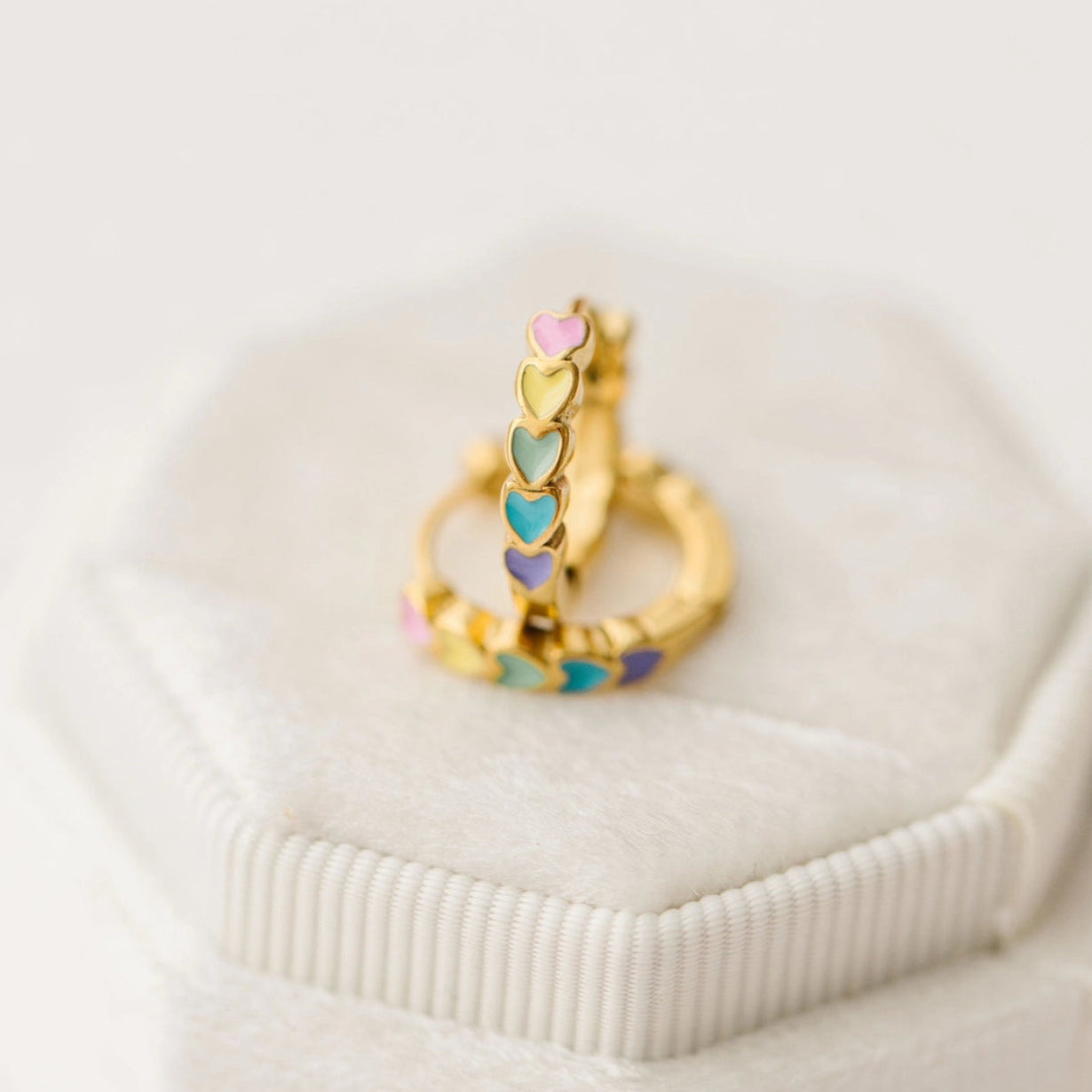 Gold ring with colorful heart-shaped stones on a white surface