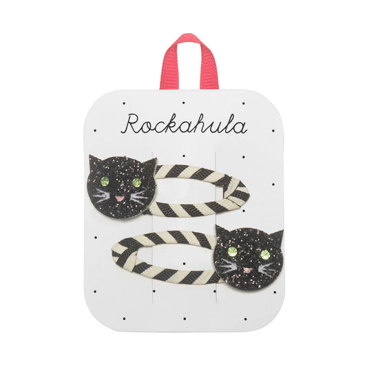 Two black and white striped hair clips with glittery black cat face charms, displayed on a white card with the name 'Rockahula' and a pink hanging loop.