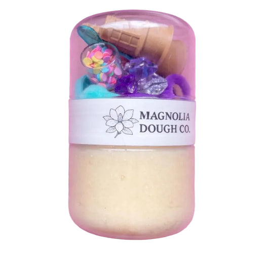 Toy dough set in a clear plastic container with 'Magnolia Dough Co.' label on a pink background