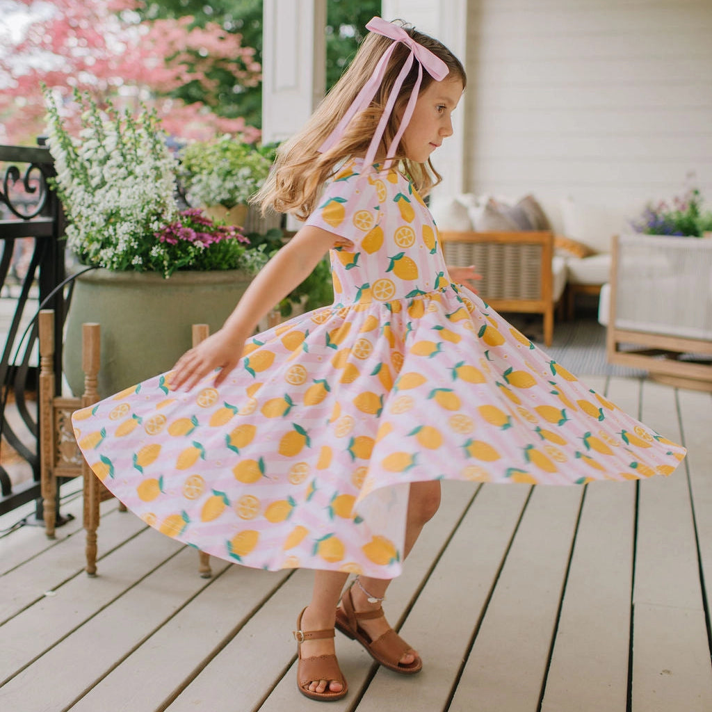 Young girl in a lemon print dress on a wooden deck with flowers and furniture in the background