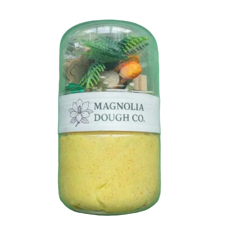 Jar of yellow dough with decorative elements on a green background, featuring Magnolia Dough Co. label.