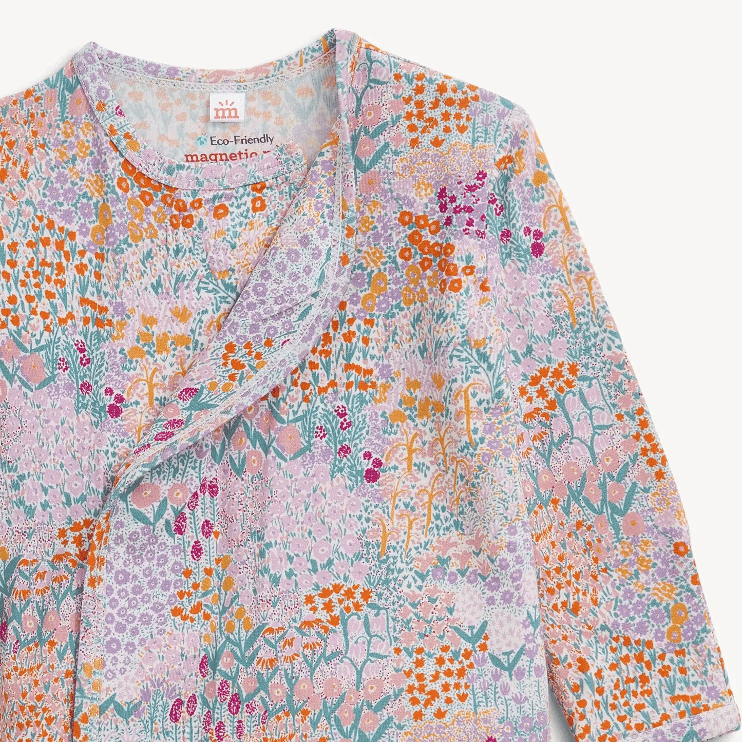 A close up of a baby gown with a colorful floral and abstract print on a light pink background.
