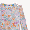A close up of a baby pajama top featuring a pink base with a floral all over print, multicolored floral pattern.