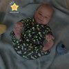 A baby lying on a textured blue blanket, wearing a long-sleeve glow-in-the-dark coverall with a green and gray dinosaur pattern on a black background.