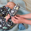 A baby wearing a navy blue and green romper with a colorful dinosaur print.