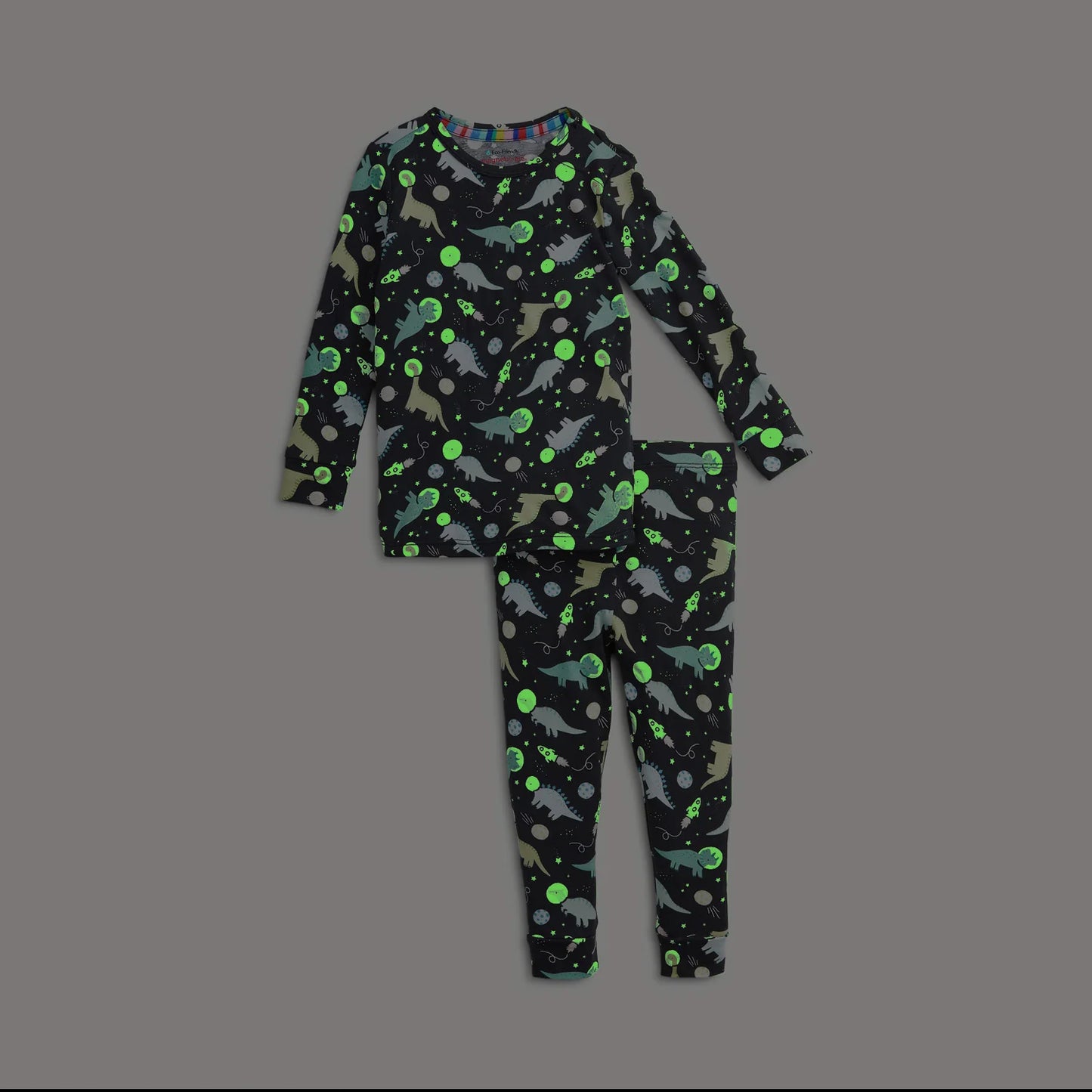 A two-piece children's pajama set featuring a long-sleeve top and matching pants with an all-over dinosaur space print on a dark gray background.