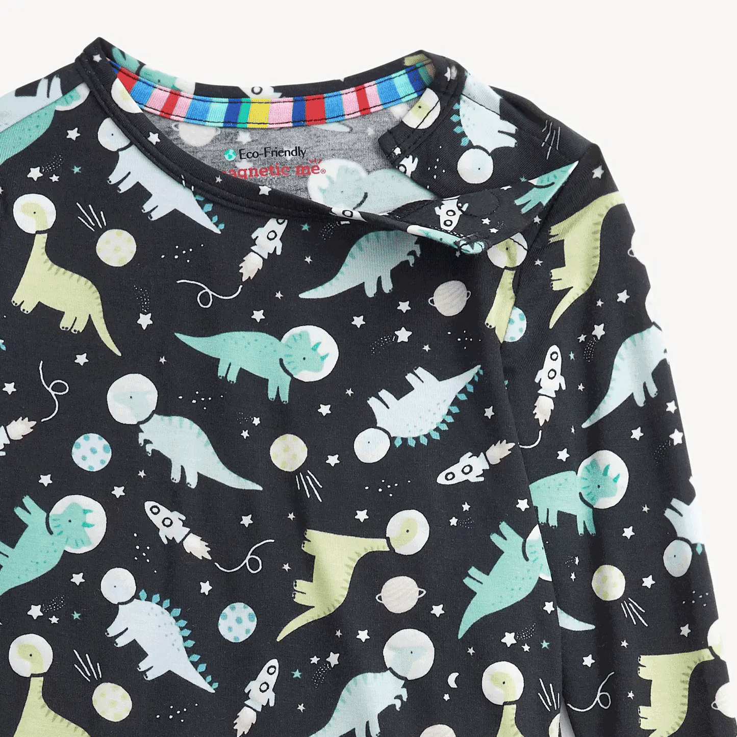 A close up of the top of a children's pajama set featuring an all-over dinosaur space print on a dark nav blue primary color.