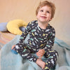 A two-piece children's pajama set featuring a long-sleeve top and matching pants with an all-over dinosaur space print on a dark gray background.