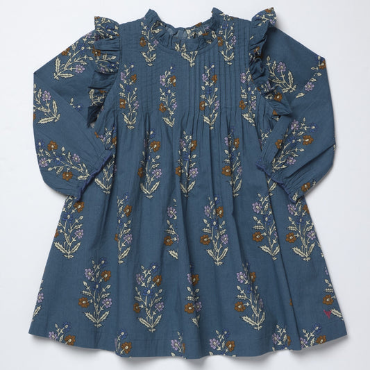 A long-sleeve blue dress with a floral print, featuring ruffled details on the shoulders and a smocked bodice, laid flat against a white background.