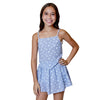 Young girl wearing a blue floral dress against a light gray background with decorative flowers.