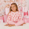 Young girl in pink pajamas sitting in front of a Christmas tree with presents.