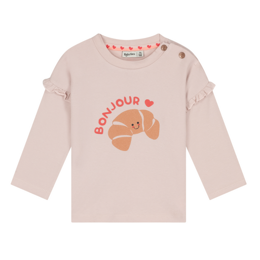 A light pink long-sleeve baby top with a croissant graphic and 'BONJOUR' text on the front, featuring ruffled cuffs and snap closures at the shoulder.