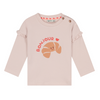 A light pink long-sleeve baby top with a croissant graphic and 'BONJOUR' text on the front, featuring ruffled cuffs and snap closures at the shoulder.