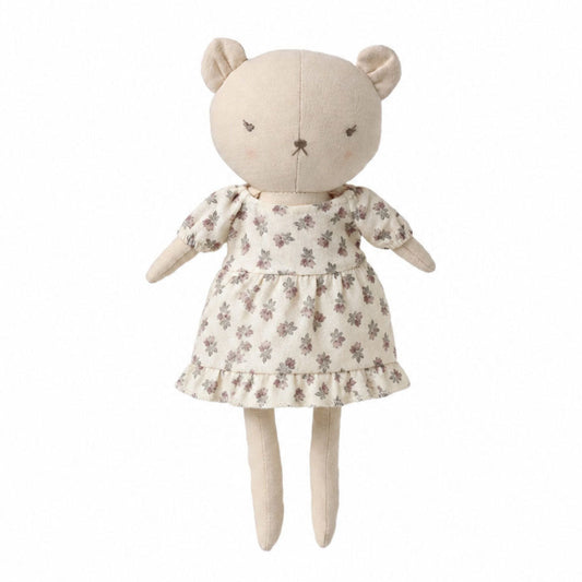 A plush teddy bear doll wearing a cream-colored dress with a small brown floral pattern, set against a plain white background.