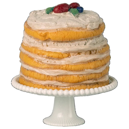 Layered cake with white frosting and fruit on top, placed on a white cake stand.