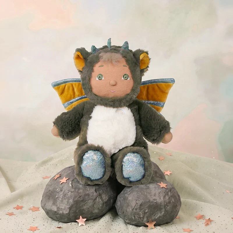 Stuffed toy dragon with a child's face sitting on a rock against a soft, blurred background.