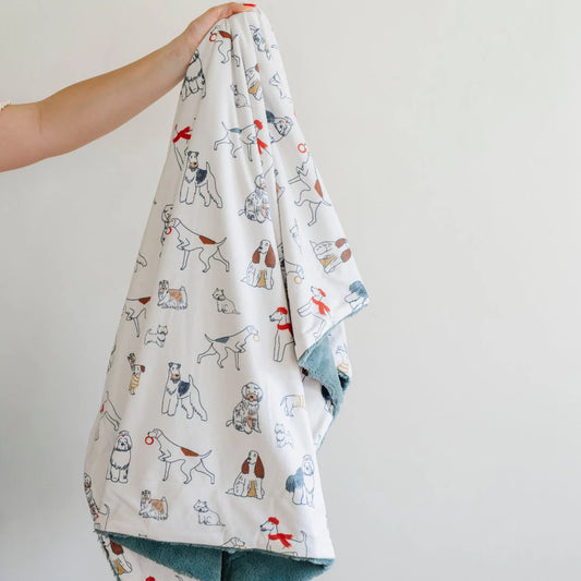 A person holding up a receiving blanket with a pattern of various cartoon dogs on a white background.