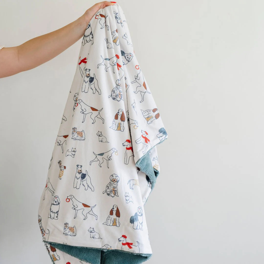 A person holding up a receiving blanket with a pattern of various cartoon dogs on a white background.