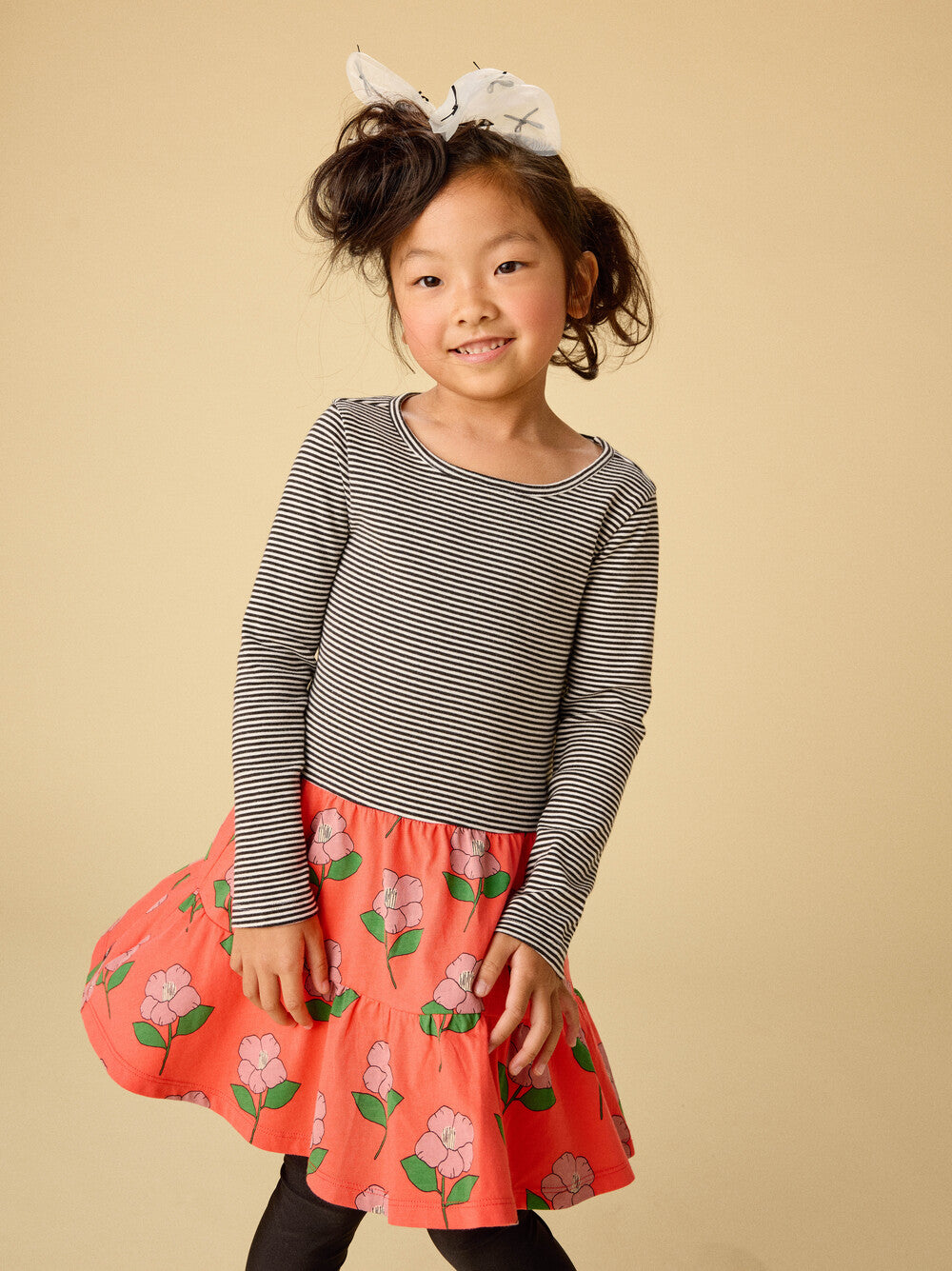 Young girl wearing a striped shirt and floral skirt against a beige background