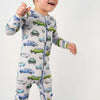 Baby wearing a car-patterned onesie and blue cap on a white background