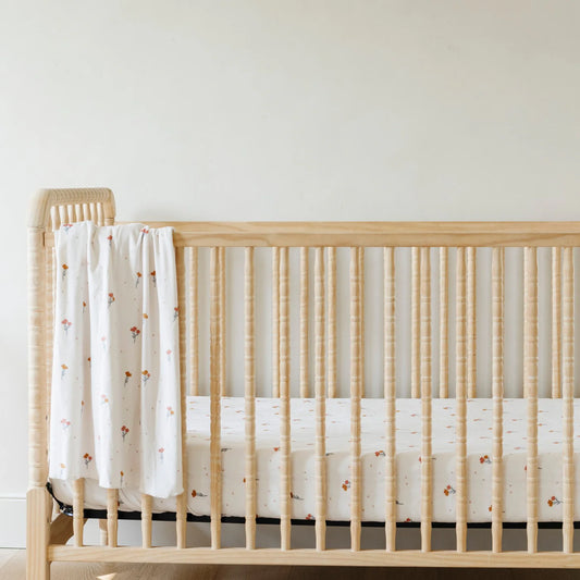 Wooden crib with a white crib sheet and blanket against a plain wall