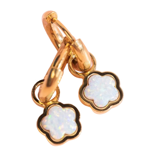 Gold charm with white opal clover-shaped pendants on a pink background