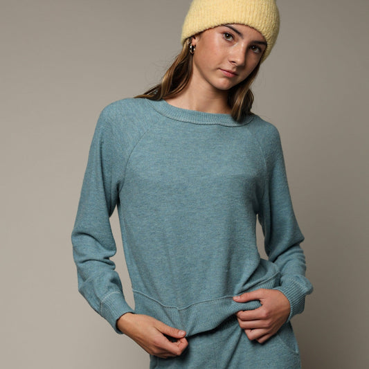 A woman modeling a heathered teal blue, long-sleeve raglan sweatshirt.
